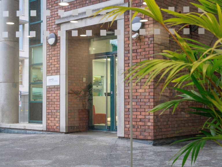 Entrance to Hayes Solicitors LLP office building with glass doors and indoor plants visible through the doorway.